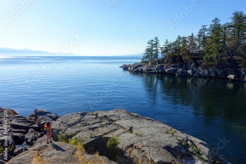A view of a little girlwalking beside an opening to a beautiful empty bay surrounded by trees and rocky shoreline,  with calm ocean water, along the sunshine coast, British Columbia, Canada photo