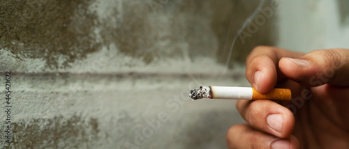 cigarette in man hand with smoke  background wall. No smoking campaign Concept.