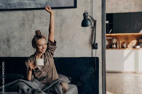 Attractive young happy female having morning coffee in bed