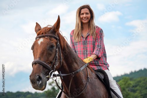 Young woman in shirt resting on brown horse - his coat wet from sweat - after riding, smiling