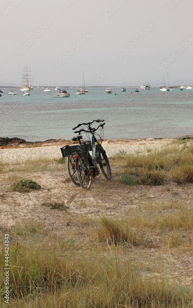 Obraz premium Bicycles on the coast of Formentera, with the sea and boats in the background. Vertical image.