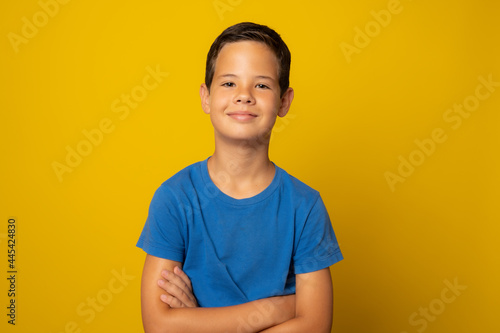 Portrait of a happy schoolboy with arms crossed, isolated on yellow. © Danko