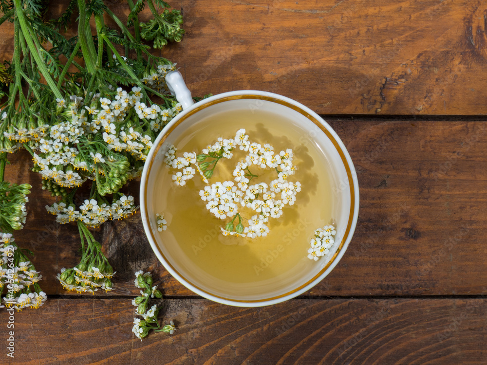 medicinal plant yarrow, a mug with a decoction of yarrow flowers on a wooden background medicinal plant yarrow, a mug with a decoction of yarrow flowers on a wooden background