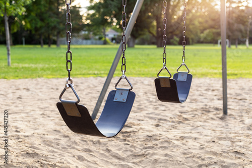 Playground for children with swings in the public park during sunset.
