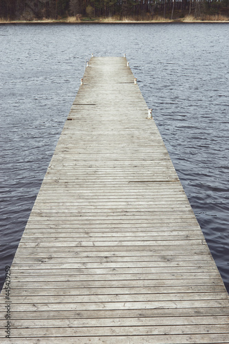 Vertical horizontal photography of wooden pier on a lake or river. Trees and forest in the background. A place of tranquility, relaxation alone with nature.