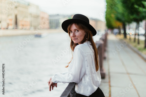 Caucasian girl in a hat walks along the embankment in the city in summer