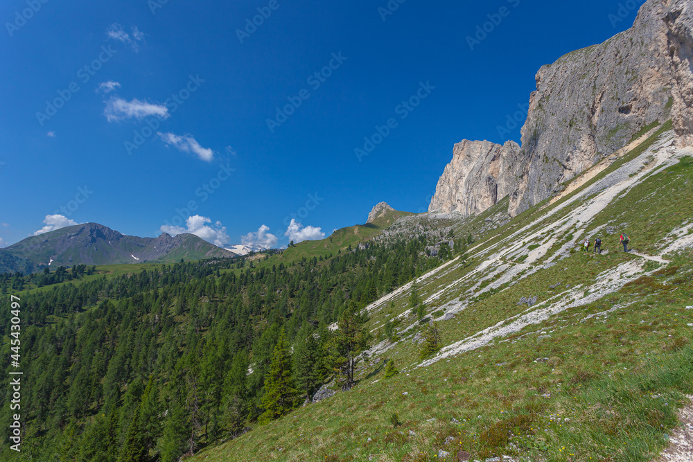 Unrecognizable people walking on a hiking trail with amazing Col di Lana Peak background, Settsass, Dolomites, Italy. The color contrasts between the different types of rocks are visible