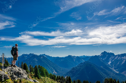 An athletic adventurous male hiker standing on top of a mountain looking out at a mountain range.