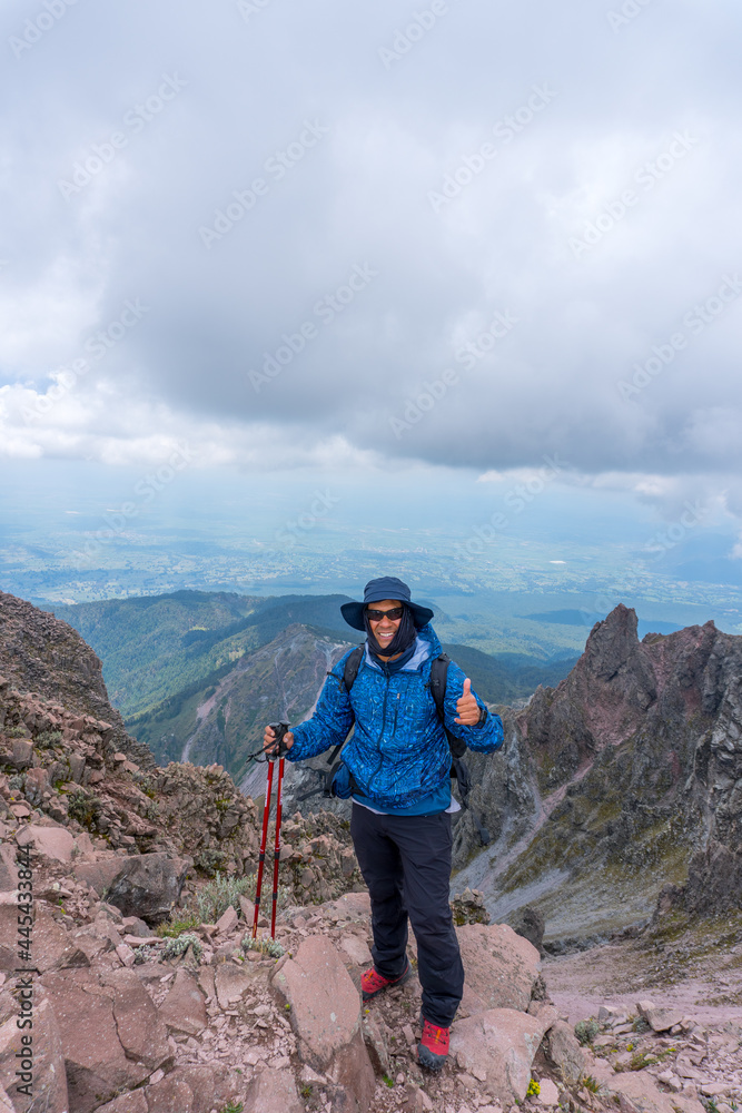 A scenic view of a Hispanic man wearing hiking clothes and posing on a cloudy sky background