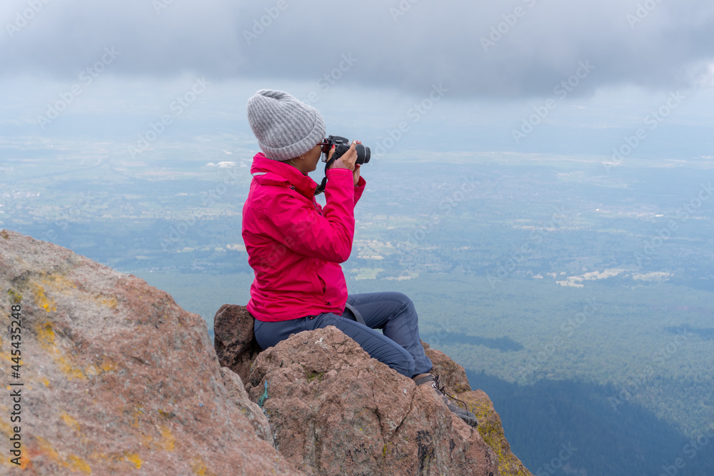 Adventurous female photographer sitting on the rock while photographing mountains