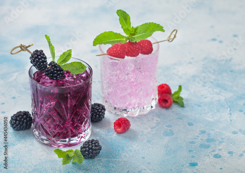 Summer cocktail with blackberry and pink lemonade in crystal glasses with ice cubes and mint on light blue background. Soda and alcohol mix.