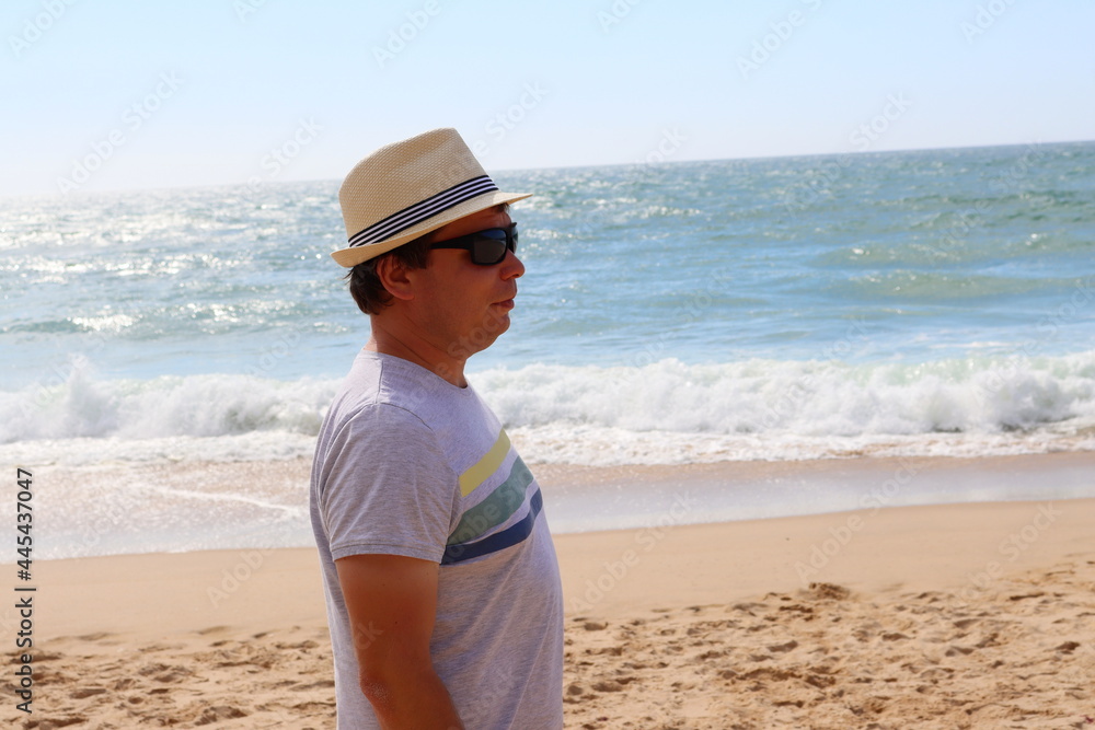 A man in profile in a hat and glasses on the background of the ocean.