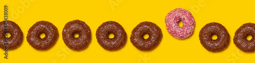 Row of brown doughnuts with single pink one standing out photo