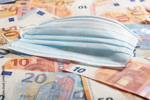 Protective face mask lying on top of pile of money symbolizing making business thanks to COVID-19 pandemic