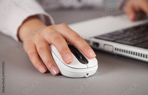 Woman's hand with computer mouse on table. White computer.