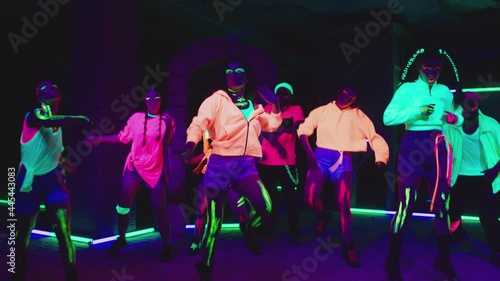 Group of female and male stylish dancers dancing inside dark place with neon lights .  Beautiful young people with fluorescent colorful make-up and clothes dancing in UV light. HD video in slow motion