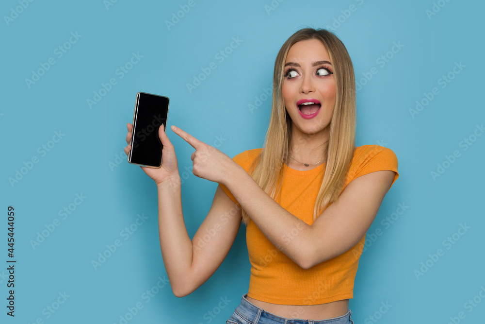 Excited Young Woman Is Holding Telephone And Pointing At It Excited Young Woman Is Holding Telephone And Pointing At It