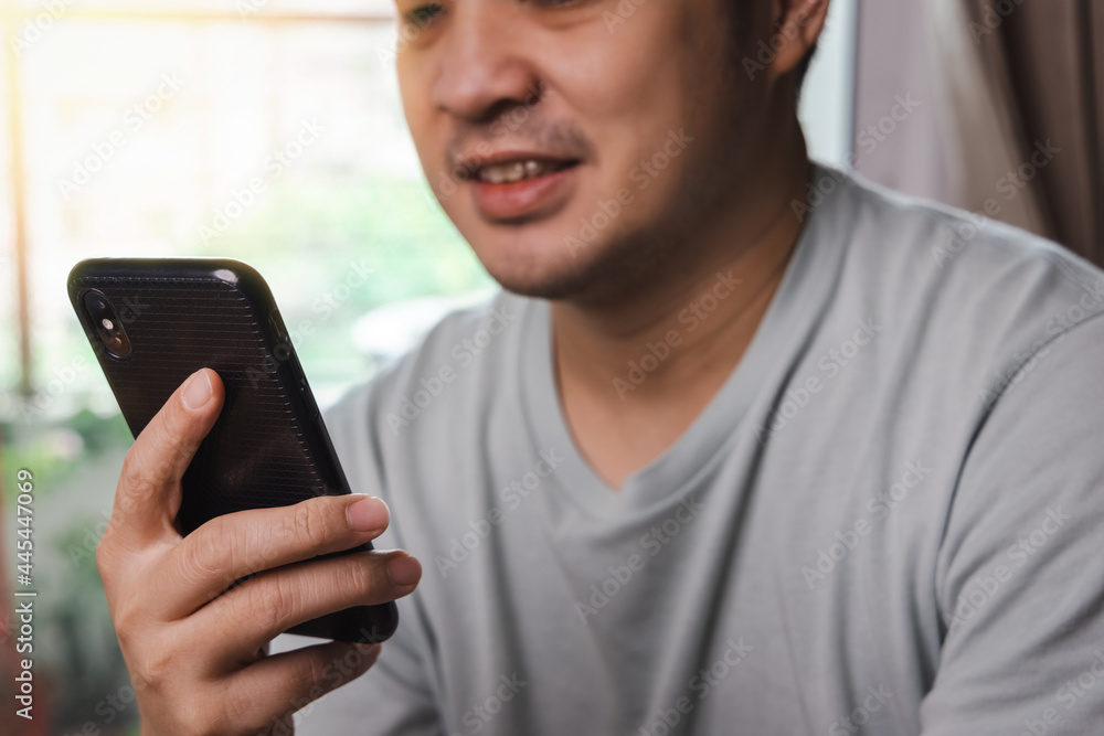 Asian adult businessman wearing shirt looking at mobile phone and smiling at his home. Work from home, business and communication technology concept. Asian adult businessman wearing shirt looking at mobile phone and smiling at his home. Work from home, business and communication technology concept.