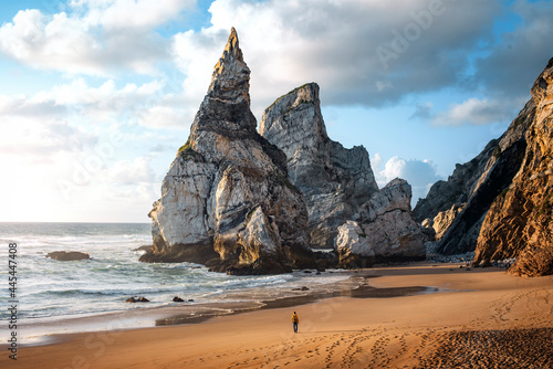 Sunset on the beach of Ursa in Sintra with a man strolling between large rocks on the coast of Portugal