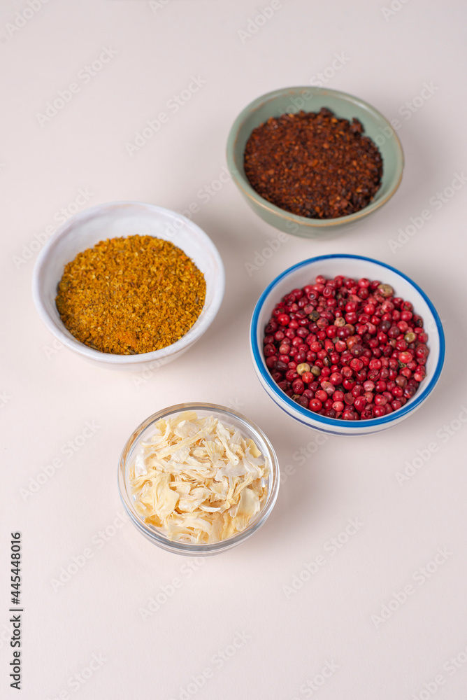 Colourful set different spices for meat, vegetarian dishes on light background. In bowls served. Seasoning pink peppercorns, dried onions, sun dried tomatoes, curry. Hot spicy background for cooking