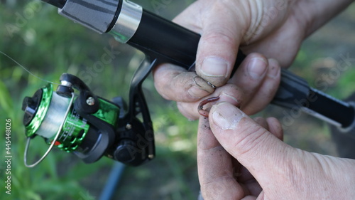 putting a worm on the hook of a fishing rod in nature close-up, male hands holding the bait and a spinning handle while preparing for fishing, leisure and fishing rest in detail