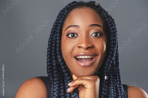 A young dark-skinned woman in a casual atmosphere looks into the camera with copy space curly black hair braided in pigtails. background color gray