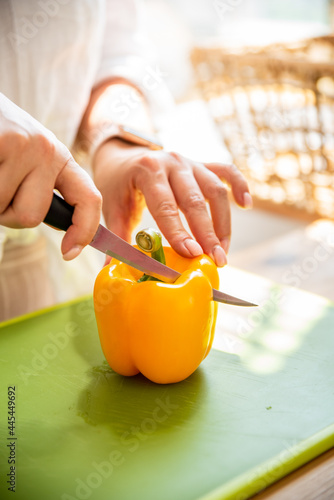 Yellow pepper is cut on a green plank. The girl prepares a summer light healthy salad. Healthy food concept
