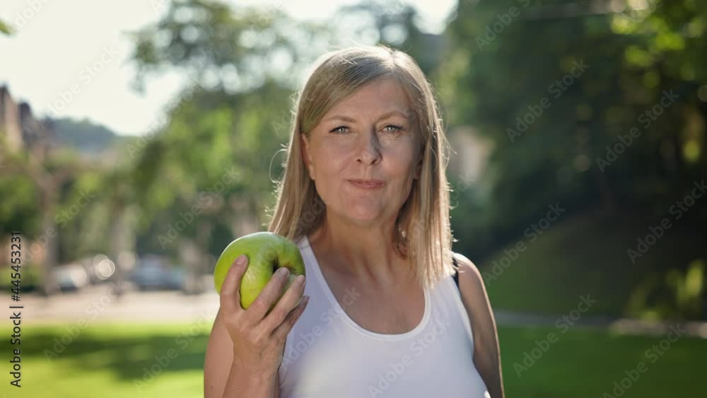 Happy Elderly Woman Holding Big Green Apple. Smiling Woman With Long Gray Hair In Park. Woman Bites An Apple And Chews. Happy Elderly Woman Holding Big Green Apple. Smiling Woman With Long Gray Hair In Park. Woman Bites An Apple And Chews.