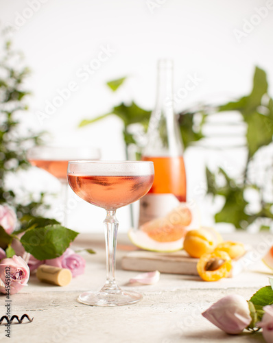Rose wine in a crystal glasses and bottle with fresh apricots,grapefruits,gentle roses and green plants on white background.Immitation of a summer sunny day.