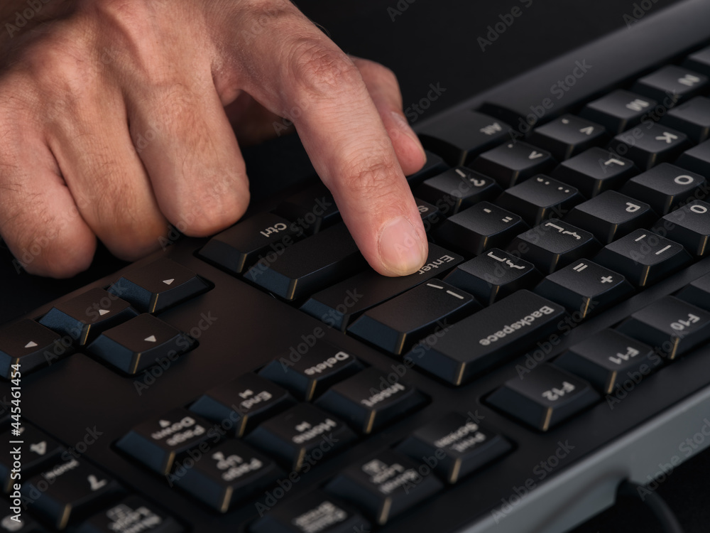 A person pressing the enter key on a black keyboard A person pressing the enter key on a black keyboard