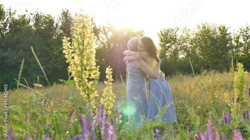 Back view of senior mother with gray hair with her adult daughter in the garden hugging each other during sunny day, sunset time outdoors, mothers day