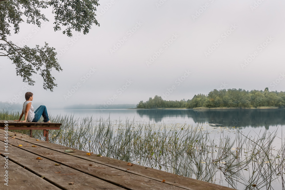 A thoughtful girl is sitting on the shore of the lake. Contemplation of the beautiful nature. Sunrise. A thoughtful girl is sitting on the shore of the lake. Contemplation of the beautiful nature. Sunrise.