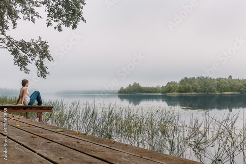 A thoughtful girl is sitting on the shore of the lake. Contemplation of the beautiful nature. Sunrise.