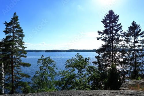 Great view over the Swedish lake Malar or Malaren. Green trees and bushes in front. Close to the cliffs or boulders. Blue sky and some clouds. Stockholm, Sweden, Scandinavia, Europe.