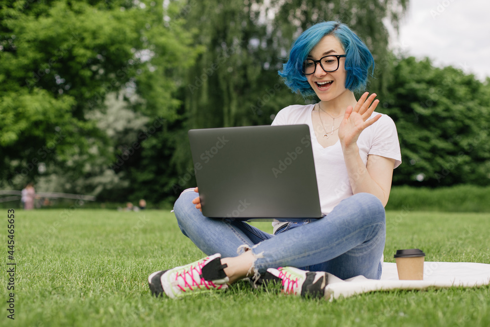 Young women with blue hair sitting on green grass with laptop in the hands. Young women with blue hair sitting on green grass with laptop in the hands.