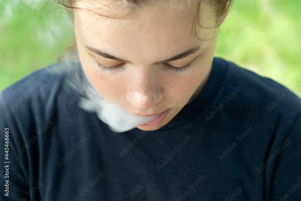 VAPE Smokes. A girl with brown hair lets off steam from her mouth in close-up. Portrait of a smoking girl. Smoking a vape cigarette to quit smoking. The concept of smoking. A bad habit. Dependence VAPE Smokes. A girl with brown hair lets off steam from her mouth in close-up. Portrait of a smoking girl. Smoking a vape cigarette to quit smoking. The concept of smoking. A bad habit. Dependence