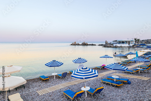 Umbrellas and sunbeds on an empty evening beach resort - vacation concept on Greece islands in Aegean and Mediterranean seas. Beach in a closed bay in a small village Charaki on a east coast of Rhodes