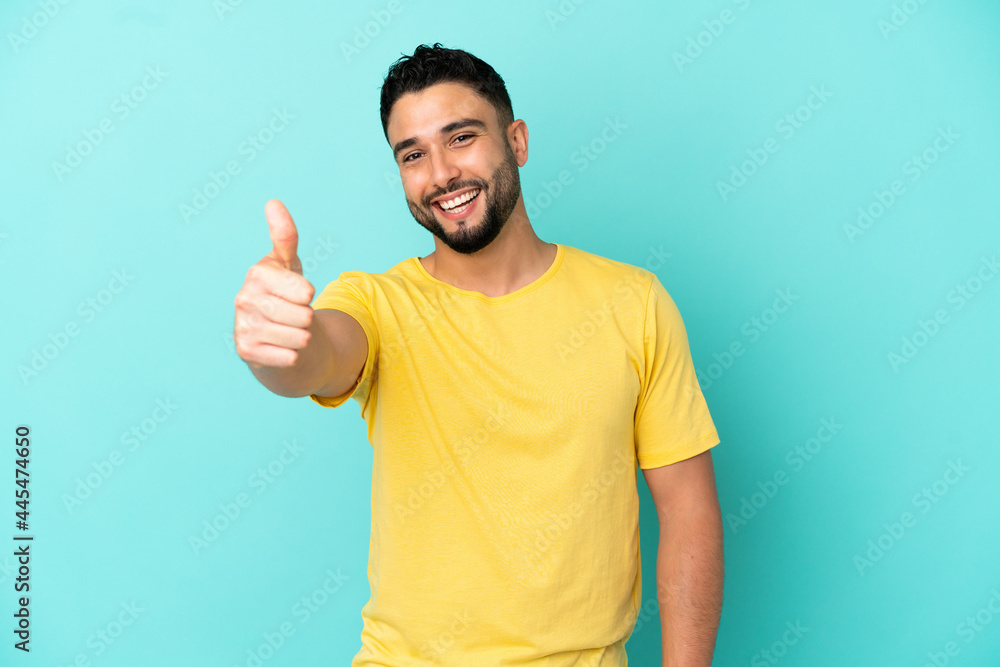 Young arab man isolated on blue background with thumbs up because something good has happened Young arab man isolated on blue background with thumbs up because something good has happened