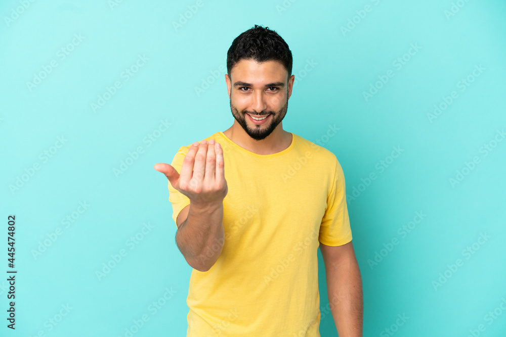 Young arab man isolated on blue background inviting to come with hand. Happy that you came Young arab man isolated on blue background inviting to come with hand. Happy that you came