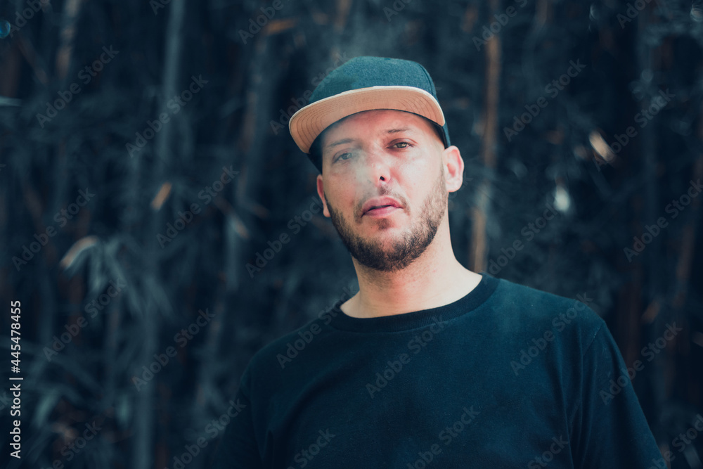 white man breathing out cigarette smoke in black t-shirt and cap outdoors white man breathing out cigarette smoke in black t-shirt and cap outdoors