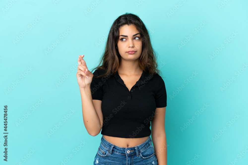 Young caucasian woman isolated on blue background with fingers crossing and wishing the best Young caucasian woman isolated on blue background with fingers crossing and wishing the best