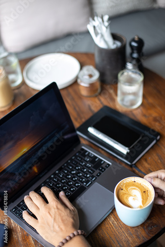 Young man using laptop in cafe near sea, freelance work, outdoor hipster portrait, smartphone, paradise island, Bali, Thailand, network, headphones, phone, breakfast at work, coffee in hand, earphones