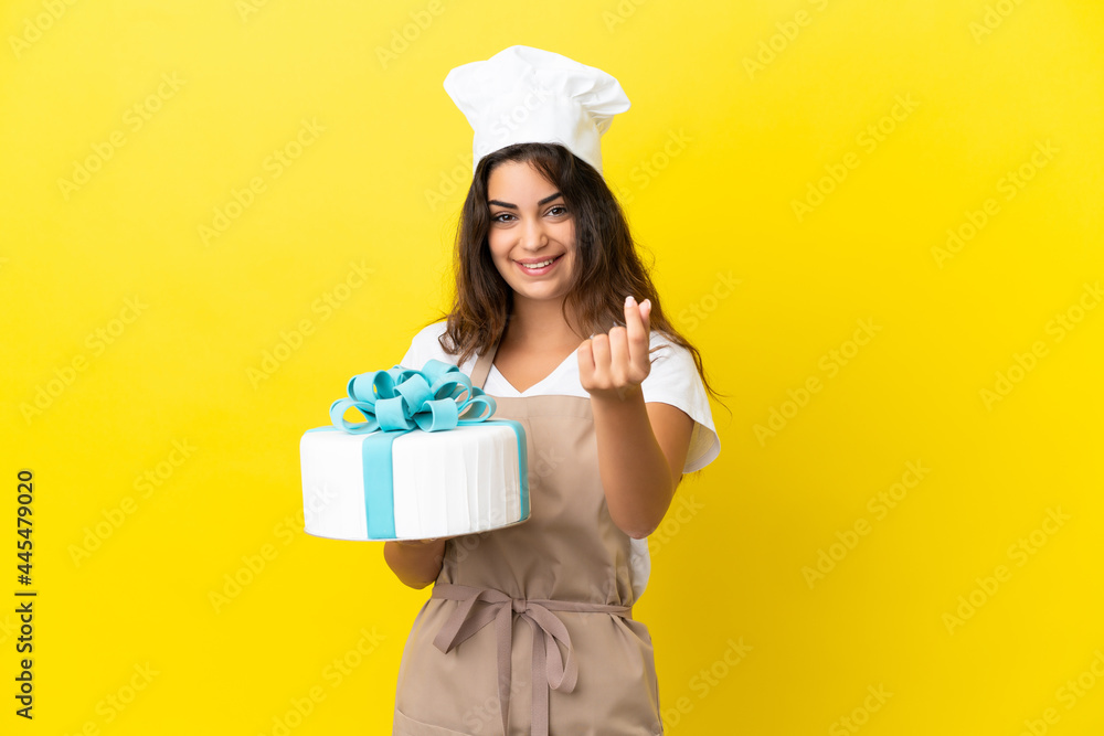 Young caucasian pastry chef woman with a big cake isolated on yellow background making money gesture Young caucasian pastry chef woman with a big cake isolated on yellow background making money gesture