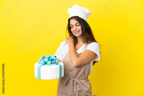 Young caucasian pastry chef woman with a big cake isolated on yellow background suffering from pain in shoulder for having made an effort