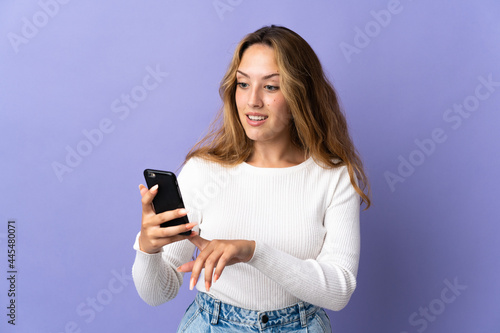 Young blonde woman isolated on purple background sending a message or email with the mobile