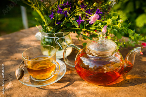 Fresh herbal tea in a clear glass teapot and cup. Wildflowers and medicinal plants on wooden table. Herbal tea in glass teapot