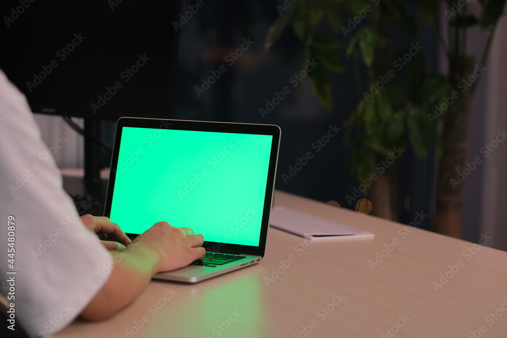 over the shoulder view of people using green screen laptop computer on table in office at night over the shoulder view of people using green screen laptop computer on table in office at night