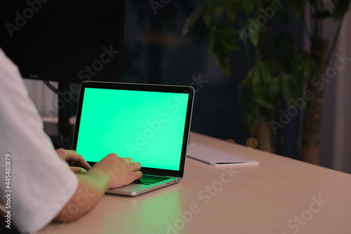 over the shoulder view of people using green screen laptop computer on table in office at night