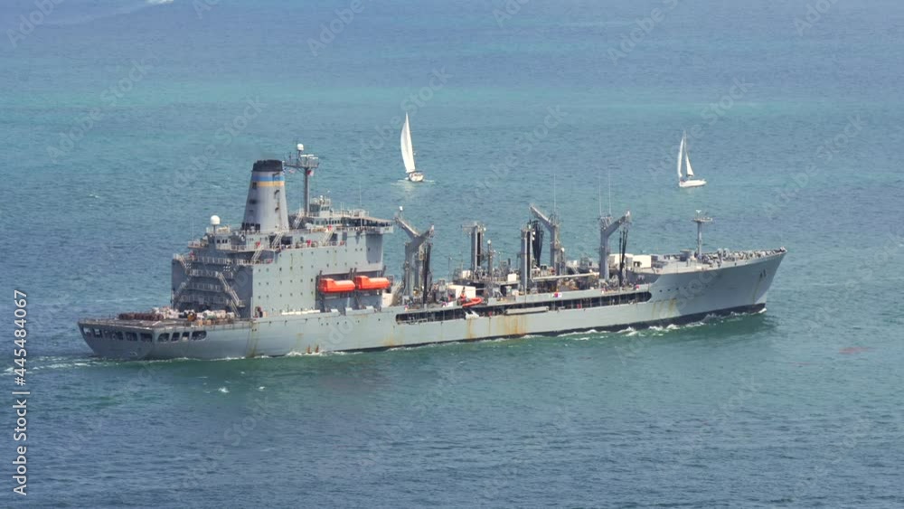 This video shows a naval ship sailing in the ocean, surrounded by sailboats and scenic blue water. This video shows a naval ship sailing in the ocean, surrounded by sailboats and scenic blue water.