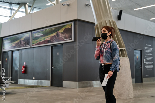 latina tourist woman with mask moving through the airport while using smart phone with social distancing during coronavirus pandemic or covid19 virus  concept of new normality